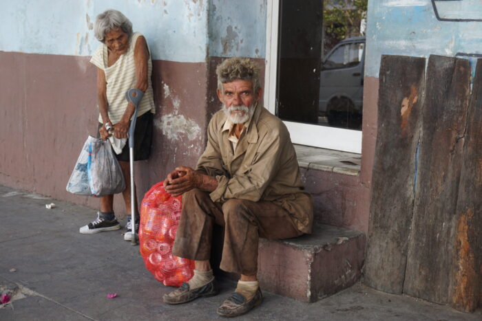 Ein alter Mann sitzt auf einer Treppe, links neben ihm eine alte Frau.