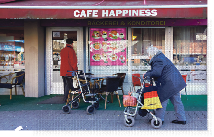 Eine Rentnerin und ein Rentner, jeweils mit Rollator, vor einem Café mit dem Namen "Cafe Happiness"