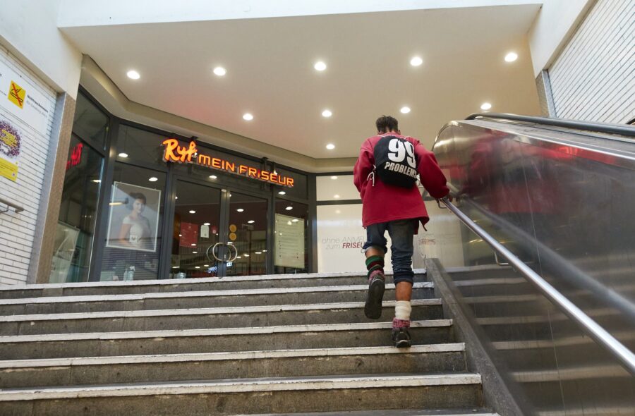 Ein Mann geht in einem Berliner U-Bahnhof die treppe hoch, er trägt einen Rucksack mit der Aufschrift "99 Problems"