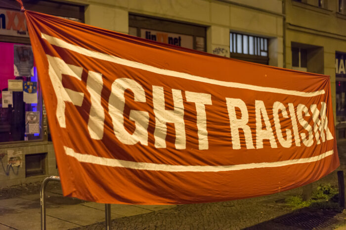 Straßenbild, vor einigen Gebäuden hängt ein großes Banner mit der Aufschrift "Fight Racism" (bekämpft Rassismus)