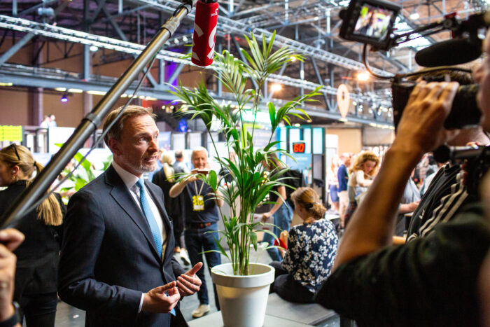 Christian Lindner steht auf der Republika 2023 vor einem Tisch und redet in ein Mikrophon, das an einer Stabverlängerung hängt. Auf dem Tisch steht eine Palme.