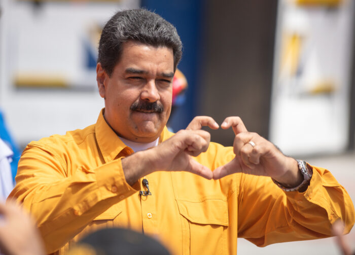 Der venezulanische Präsident Nikolas Maduro formt, gekleidet in ein senfgelbes Hemd, ein Herz mit seinen Fingern in Richtung Publikum. Das Bild zeigt ihn in einer nahen Aufnahme, im Juli 2024 bei einer Rede vor der revolutionären Jugend seiner Partei