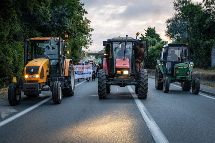 Drei Traktoren fahren auf einer Straße, hinter ihnen die Spitze eines Demonstrationszuges.