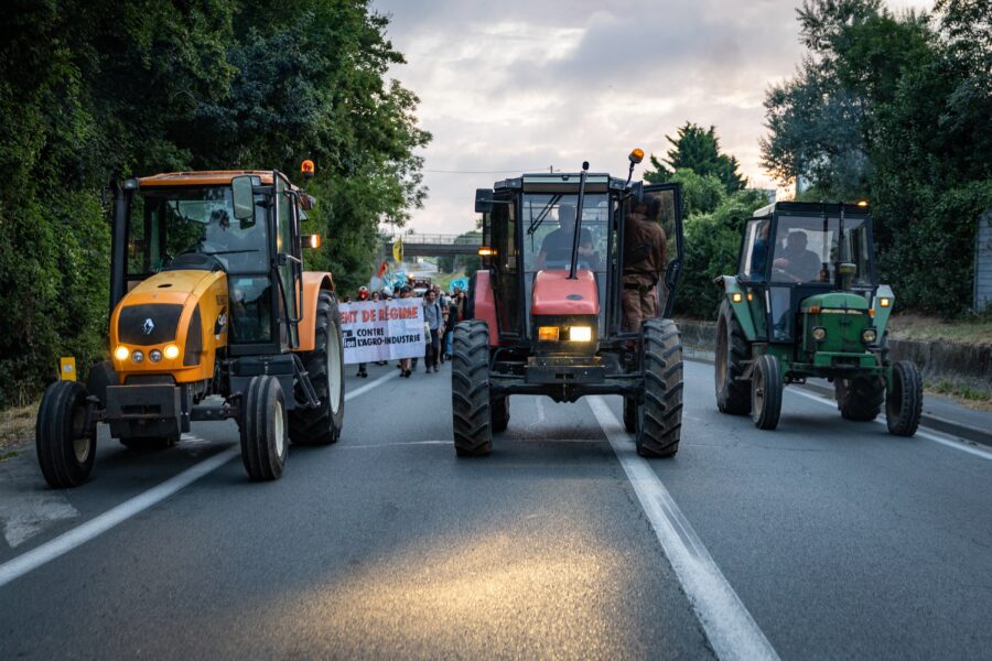 Drei Traktoren fahren auf einer Straße, hinter ihnen die Spitze eines Demonstrationszuges.