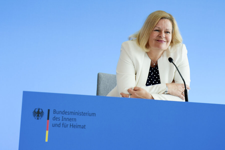 Man sieht auf dem Bild Innenministerin Nancy Faeser bei einer Pressekonferenz. Sie grinst.