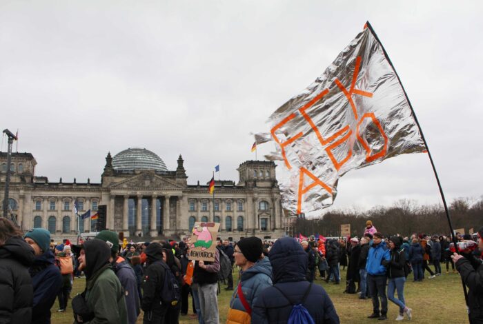 Man sieht Leute vor dem Bundestag stehe. Auf einer glitzernden Fahne steht "FCK AfD".