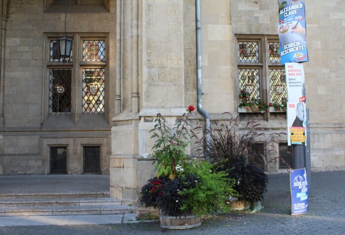 Ein Blumenkübel vor dem Erfurter Rathaus, daneben ein Laternenmast mit Wahlplakaten der AfD, der Linkspartei und der FDP