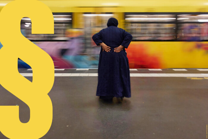 Foto einer Fahrenden Ubahn in einer Station, davor eine ältere Frau, die sich den Rücken hält.