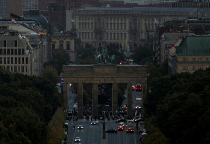 Blick von oben auf das Brandenburger Tor bei Dämmerung. Im Vordergrund sind noch ein Teil der Straße des 17. Juni zu sehen, im Hintergrund weitere Gebäude.