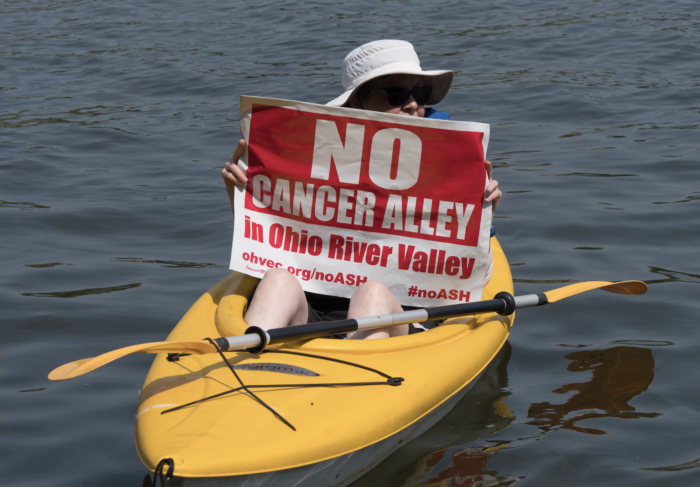 Eine Person in einem kleinen Boot, die ein Schild mit der Aufschrift "No Cancer Alley" in der Hand hält.