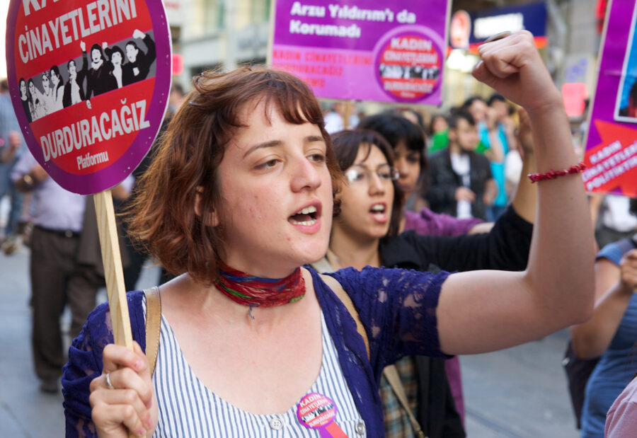 Aktivist*innen der Plattform "Wir werden Frauenmorde stoppen" protestieren mit Schildern und erhobenen Fäusten.