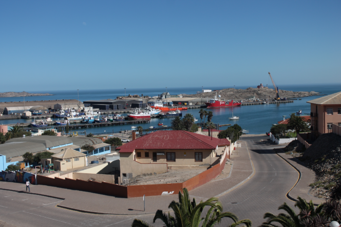 Sicht Shark Island, einer felsigen Halbinsel. Davor ankern Schiffe an einem Hafen, der vor der Halbinsel liegt.