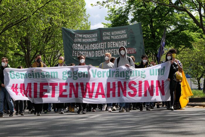 Die Spitze eines Demonstrationszuges (wegen der Corona-Pandemie tragen die Teilnehmer*innen noch Masken); auf dem Banner steht "Mietenwahnsinn"