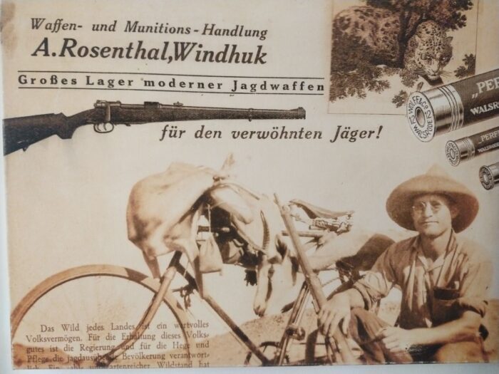 Foto einer alten Relkame für einen Waffenhandel. Ein Jäger posiert mit einem geschossenen Tier auf seinem Fahrrad hinter ihn.