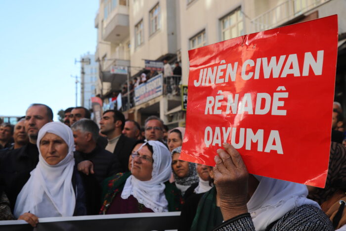 Menschen beim Protest in Mêrdîn gegen die Absetzung kurdischer Bürgermeister*innen im November 2024. Jemand hält ein Schild hoch mit der Aufschrift "Jinên ciwan rê nadê qayuma" (»Junge Frauen werden die Zwangsverwaltung nicht zulassen«).