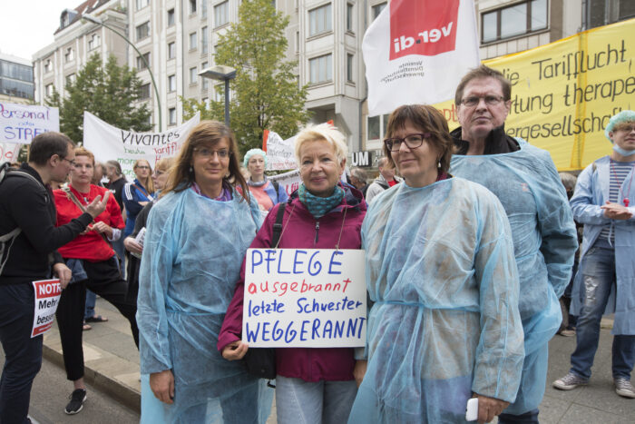 Man sieht vier Personen, die Pflegekleidung tragen und ein Schild hochhalten, auf dem steht: Pflege ausgebrannt, letzte Schwester weggerannt.