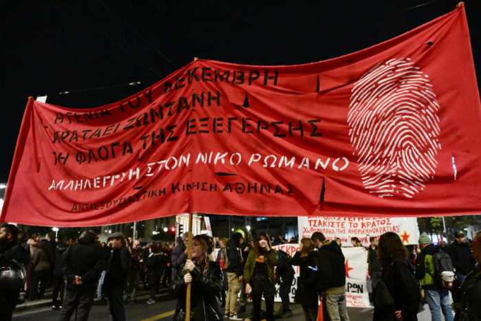 Demonstrant*innen tragen ein rotes Transparent mit einer ufschrift in Griechisch