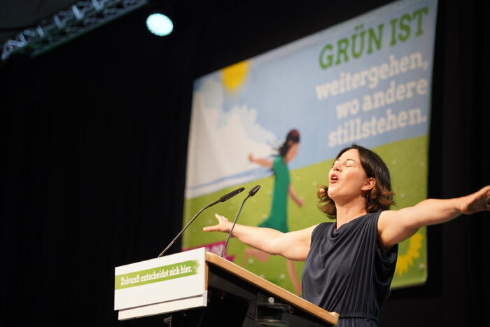 Das Bild zeigt Außenministerin Baerbock Annalena an einem Redepult stehend und die Arme ausbreitend. Sie hat die Augen geschlossen. Hinter ihr ist ein Plakat mit Wahlwerbung für die grüne Partei zu sehen