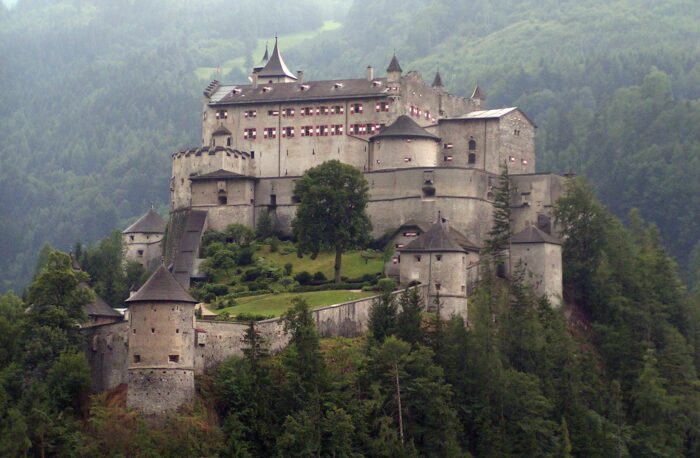 Eine Burg auf einem bewaldeten Hügel, die Fensterläden sind rotweiß