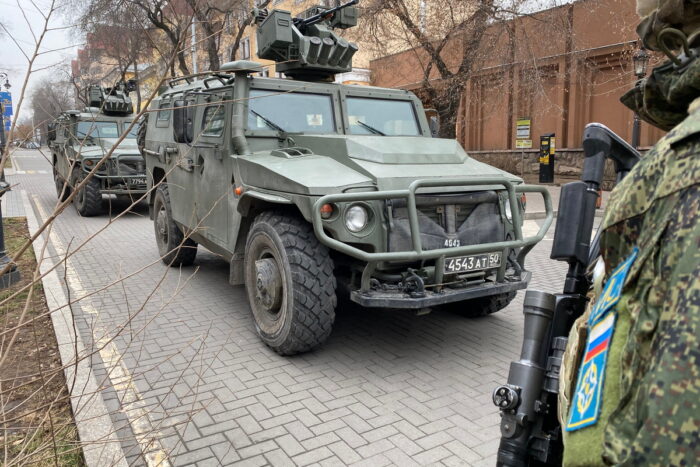 Zwei gepanzerte Militärfahrzeuge hintereinander auf einer Straße, von vorne fotografiert, rechts vorne im Bild ein Soldat mit Waffe