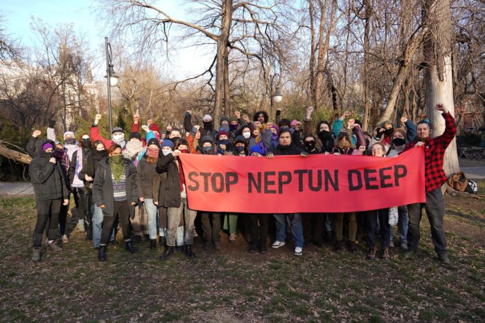 Ein Gruppe teils vermummter Protestierender hält ein rotes Banner mit der Aufschrift "Stop Neptun Deep".