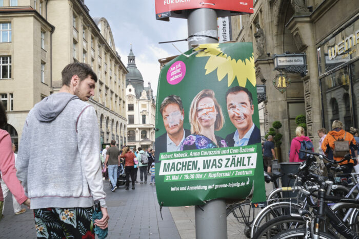 Ein Mann geht in der Leipziger Innenstadt an einem Wahlplakat der Grünen vorbei und schaut das Plakat angewidert an.