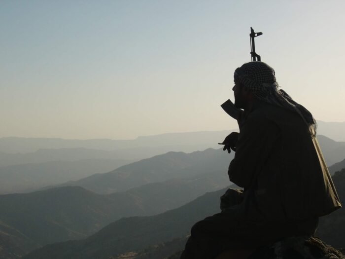 Silhouette eines PKK-Kämpfers mit einer Waffe und einer Zigarette in der Hand, im Hintergrund Berge