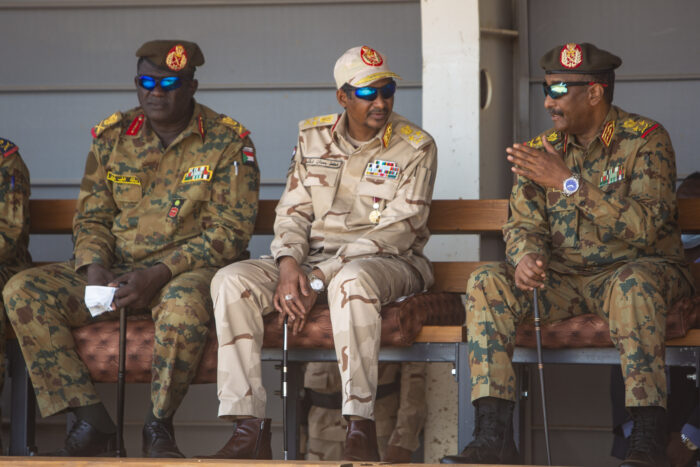 Foto von drei hochrangigen Soldaten, sitzen und in Uniform. Die zwei rechts in Bild unterhalten sich miteinander.